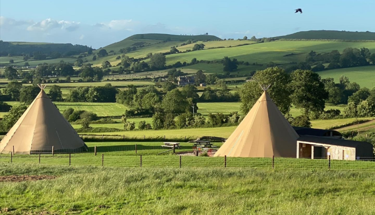 Two teepees in a field with the Dorset countryside in the background
