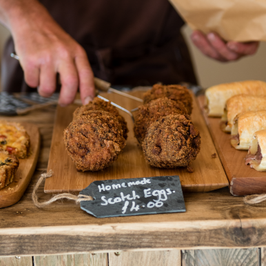 Homemade scotch eggs on a wooden board, being picked up by a man in an apron